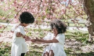 Madre e hija con vestido blanco y cabello chino. En un campo, bajo la sombra de un árbol.
