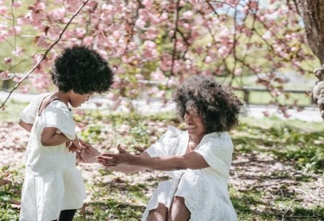 Madre e hija con vestido blanco y cabello chino. En un campo, bajo la sombra de un árbol.